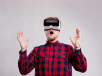 Man wearing virtual reality goggles. Studio shot, gray backgrou